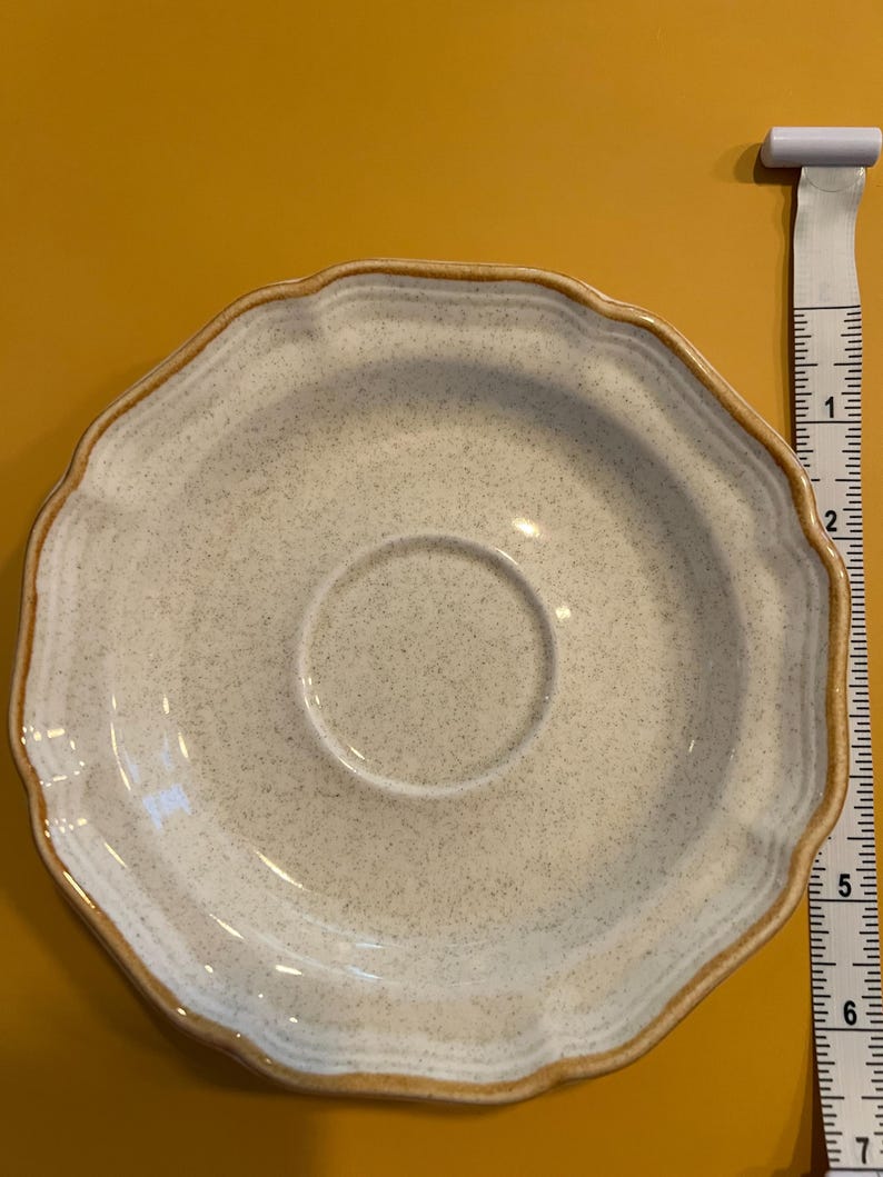 Pu&ograve; includere: Un piattino in ceramica bianco sporco maculato con bordo smerlato e rifinitura marrone. Il piattino ha un diametro di circa 14 cm. Il centro ha un'area incassata per una tazza da t&egrave;.