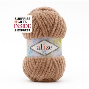 May include: A large ball of tan Alize Soffy Mega yarn. The yarn is thick and fluffy, with a soft texture. The label reads "alize" and "Soffy Mega". The image also includes text that reads "SURPRISE GIFTS INSIDE & EXPRESS".