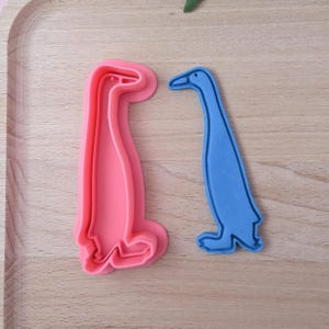 Op de afbeelding: Twee koekjesvormen, een roze en een blauwe, in de vorm van een staande pinguïn.