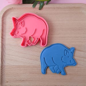 Könnte beinhalten: Zwei Keksausstecher in Form eines Wildschweins aus Kunststoff. Der Ausstecher links ist rosa und der Ausstecher rechts ist blau.