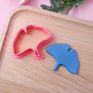 Könnte beinhalten: Ein rosa Plastik-Ausstecher in Form eines Ginkgoblattes und ein blaues Ginkgoblatt aus Modelliermasse.