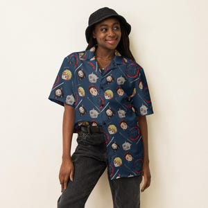 May include: Navy blue button-down shirt with a repeating pattern of anime character faces and Japanese text. The short-sleeved shirt features a collared neckline and is worn with black pants and a black bucket hat.