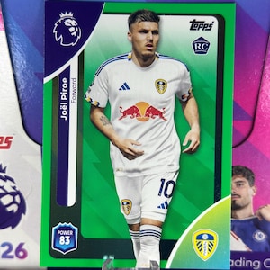 Pode incluir: Um cartão colecionável Topps da Premier League com Joël Piroe, avançado do Leeds United. O cartão tem uma borda verde e mostra o jogador com seu uniforme branco e azul. O cartão também mostra o logotipo da Premier League e uma potência de 83.