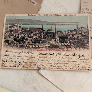 Könnte beinhalten: Alte Postkarte von Konstantinopel mit Panoramablick auf die Stadt mit Moscheen und Minaretten. Die Postkarte hat handschriftlichen Text und ist von anderen alten Papieren umgeben, was auf ein historisches Thema hindeutet.
