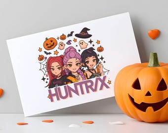 May include: A white card featuring a Halloween-themed illustration of three anime-style girls with pumpkins, bats, and a witch hat. The card has the text "HUNTR/X" in purple. An orange carved pumpkin and Halloween confetti are in the foreground.