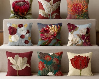 May include: A collection of nine square throw pillows featuring diverse botanical and floral prints. The designs include red protea flowers, white banana leaves, orange spider lilies, multi-colored floral clusters, and single large red tulips.