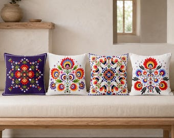 May include: Four square throw pillows featuring vibrant, symmetrical folk-art floral patterns. The first is dark purple, the second and fourth are white with red and blue flowers, and the third is white with a central mandala-style rooster design.