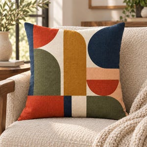 Könnte beinhalten: Ein quadratisches Zierkissen mit einem geometrischen Muster aus Halbkreisen und Rechtecken in den Farben Marineblau, Senfgelb, Olivgrün, Terrakotta-Orange und Creme. Der Stoff weist durchgehend eine sichtbare leinenartige Textur auf.