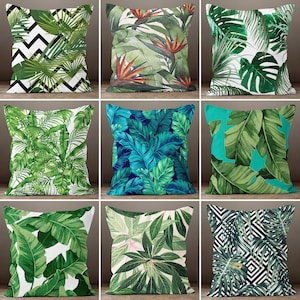May include: Nine decorative throw pillows with tropical leaf designs. The pillows feature various patterns, including green leaves on white, blue leaves, and geometric designs. The pillows are square and likely made of fabric.