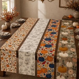 Op de afbeelding: Vier lange rechthoekige tafellopers op een houten tafel. Elke loper heeft een herfstachtig patroon, waaronder oranje pompoenen met herfstbladeren, zwart-witte lijntekeningen van pompoenen, blauwe en oranje pompoenen en witte pompoenen.