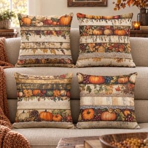Peut inclure: Quatre coussins carrés décoratifs avec un motif de récolte composé de bandes horizontales de citrouilles, de feuilles d'automne, de baies et d'une bordure en dentelle. Les tons incluent orange, marron, crème et vert sur un tissu texturé.