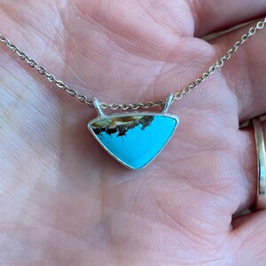 May include: A silver chain necklace with a turquoise and brown triangular pendant.