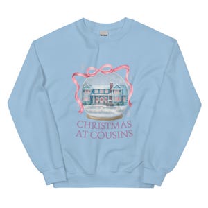 Peut inclure: Sweat-shirt bleu clair avec un motif de boule à neige représentant une maison, un nœud rose et le texte "CHRISTMAS AT COUSINS" en rose. Ce vêtement confortable est parfait pour la saison des fêtes.