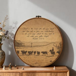 May include: A round wooden wall art piece featuring a sepia-toned western landscape with a cowboy on horseback herding cattle. The artwork includes the text "Trust in the Lord with all your heart..." from Proverbs 3:5-6.