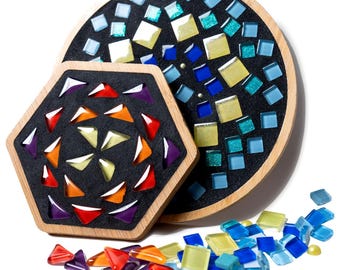 May include: A circular wooden tray and a hexagonal wooden tray, both filled with black grout and inlaid with colorful glass mosaic tiles. The circular tray features blue, yellow, and teal squares, while the hexagonal tray has red, orange, and purple triangles. Loose glass tiles are scattered below.