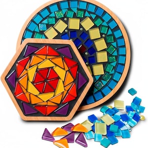 May include: Two mosaic coasters with wooden frames. One is round, the other is hexagonal. Both feature colorful glass tiles in shades of blue, green, yellow, orange, red, and purple. Loose tiles are scattered nearby.