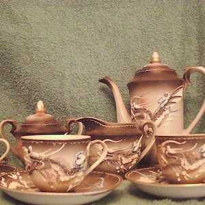 May include: A vintage tea set with a brown and cream color scheme. The set includes a teapot, creamer, sugar bowl, and several teacups and saucers. Each piece is decorated with a dragon motif.