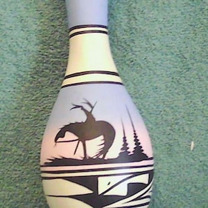 May include: A white and blue ceramic vase with a Native American design. The vase features a black silhouette of a horse and rider against a blue and pink background. Black geometric patterns and lines decorate the vase.