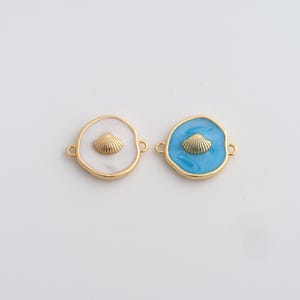 Peut inclure: Deux breloques rondes dorées avec un motif de coquillage. L'une a un fond en émail blanc, l'autre est bleu clair. Les deux ont un coquillage doré au centre et de petites boucles pour les attacher à une chaîne ou un bracelet.