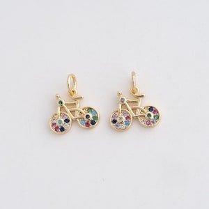 May include: Two gold-colored bicycle charms with colorful gemstone accents on the wheels. The charms have a loop at the top for attaching to a necklace or bracelet. The bicycle frames are detailed and delicate.