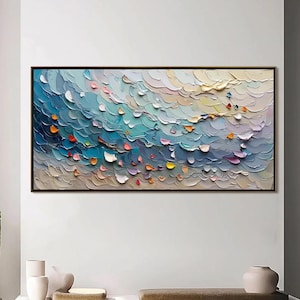 May include: Abstract oil painting in a black frame. The artwork features a textured, layered design with shades of blue, teal, white, and touches of orange, pink, and yellow. The painting is displayed on a white wall above a bench.