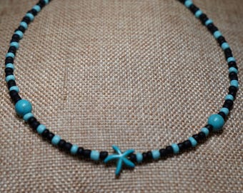 Peut inclure: Un collier de perles avec des perles noires et turquoise et un fermoir argenté. Le collier comporte un pendentif étoile de mer turquoise et deux perles turquoise. Le collier est présenté sur un fond neutre.