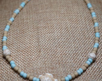 Peut inclure: Un collier de perles avec des perles bleu clair et beige alternées. Le collier comprend trois breloques en forme de tortue blanches. Le collier est sécurisé par un fermoir argenté.