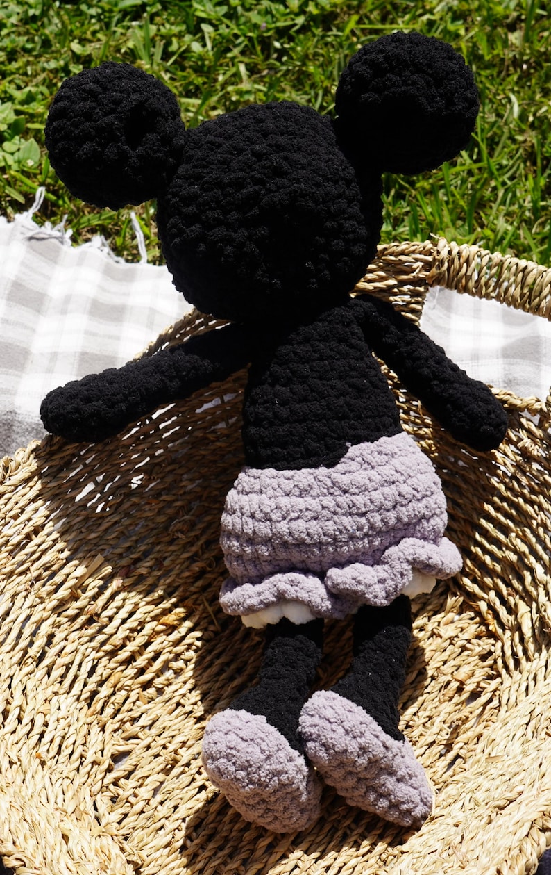 May include: A handmade black and gray crochet doll with large round ears, arms, and legs. The doll has a gray skirt with a ruffled hem and is sitting in a woven basket. The doll's feet are gray and black.