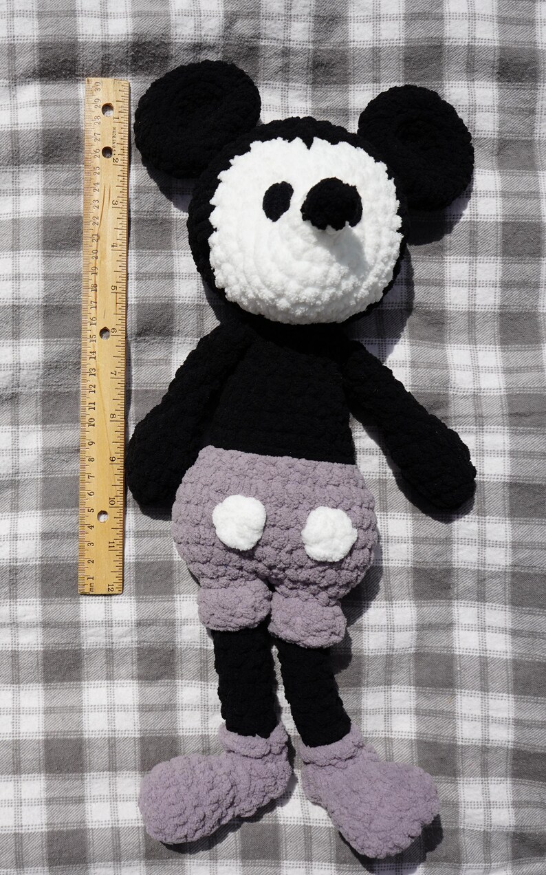 May include: A handmade crochet Mickey Mouse doll. The doll features a white face, black ears, arms, and legs, and gray shorts with white buttons. The doll is approximately 18 inches tall.