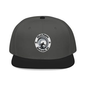 Puede incluir: Gorra gris y negra de ala plana con un parche bordado. El parche dice "Ditch Plains Montauk, NY" y muestra a un surfista en una ola. La gorra tiene una visera negra y un botón en la parte superior.