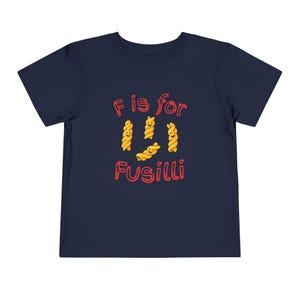 May include: Navy blue toddler t-shirt with the text "F is for Fusilli" in red, featuring cartoon fusilli pasta. The pasta is yellow with smiling faces. A fun and playful design for kids.