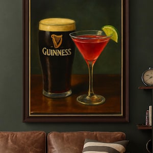 K&ouml;nnte beinhalten: Gerahmtes Gem&auml;lde mit einem Pint Guinness und einem roten Cocktail mit Limettenscheibe. Das Guinness-Glas zeigt den Markennamen und das Harfenlogo. Das Bild hat einen dunkelgr&uuml;nen Hintergrund.