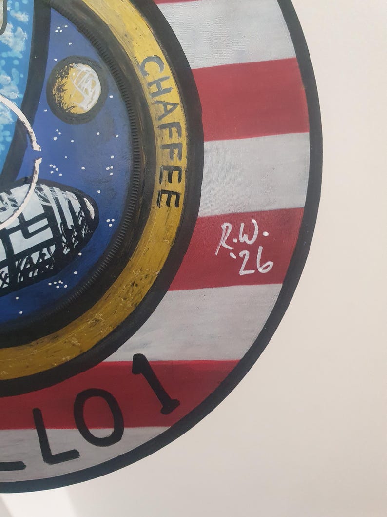 K&ouml;nnte beinhalten: Rundes Gem&auml;lde mit dem Apollo 1 Missionsabzeichen. Das Design zeigt ein Raumschiff, einen Planeten und einen Sternenhimmel. Der Rand ist gelb mit dem Namen "CHAFFEE" in Schwarz. Der Hintergrund hat rote und wei&szlig;e Streifen, mit der Nummer "01" in Schwarz.