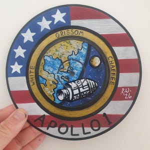 K&ouml;nnte beinhalten: Handgemalte Apollo 1 Gedenkkunst auf einer kreisf&ouml;rmigen Oberfl&auml;che. Das Design zeigt die amerikanische Flagge, Sterne und Streifen, mit den Namen "Grissom, White, Chaffee" und dem Wort "Apollo 1". Eine detaillierte Illustration eines Raumschiffs ist ebenfalls enthalten.