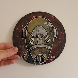 May include: Hand-painted artwork on a circular surface, featuring a robot-like character with a detailed helmet in shades of olive green, gray, and gold. The background is a deep red with white speckles. Signed "R.W. '26".