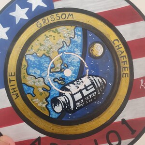 K&ouml;nnte beinhalten: Handbemalte Schallplatte mit einem Apollo 1 Missionsdesign. Das Kunstwerk zeigt einen Hintergrund mit der amerikanischen Flagge, eine Darstellung der Erde, ein Raumschiff und die Namen "Grissom", "Chaffee" und "White". Die Schallplatte ist ein einzigartiges Kunstwerk zum Thema Weltraum.