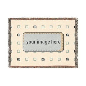 May include: Cream-colored woven throw blanket with a repeating pattern of small cameras and squares. The center features a rectangular patch with the text "your image here". The blanket has a fringed edge.