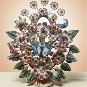 Może przedstawiać: Ręcznie wykonana metalowa rzeźba drzewa z postarzanym wykończeniem. Rzeźba przedstawia kwiaty w odcieniach czerwieni, bieli i brązu, z zielonymi liśćmi i niebieskim motylem. Drzewo jest zamontowane na białej podstawie.