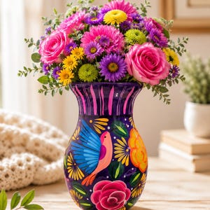 May include: A dark purple ceramic vase featuring hand-painted designs of a blue and pink bird, orange flowers, and a large pink rose. The vase is filled with a vibrant bouquet of pink roses, yellow daisies, purple asters, and green chrysanthemums.