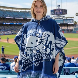 May include: A blue and white poncho featuring the Los Angeles Dodgers logo and a Hello Kitty design. The poncho has a hood and fringe along the bottom. The image is taken at a baseball stadium.