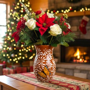 May include: A brown ceramic vase with a white floral pattern and a butterfly design, filled with a festive arrangement of red poinsettias, white roses, and greenery. The vase sits on a table with a patterned runner.