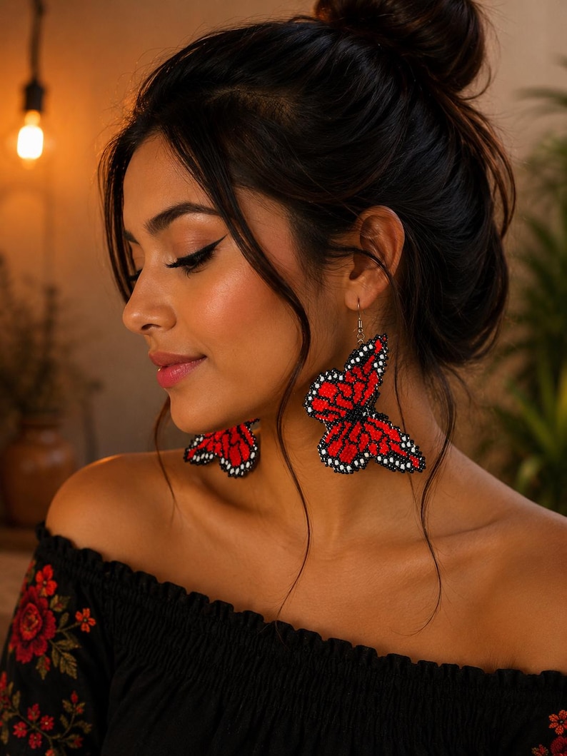 Op de afbeelding: Rode en zwarte kralen vlinder oorbellen. De oorbellen zijn felrood met zwarte details, gevormd als vlinders. De oorbellen worden gedragen met een zwarte off-the-shoulder top met rode bloemenborduurwerk.