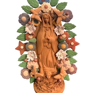May include: A terracotta-colored religious statue of a woman, surrounded by colorful flowers, butterflies, and leaves. The statue has a detailed design and is set against a white background. The flowers are in shades of blue, pink, and orange.