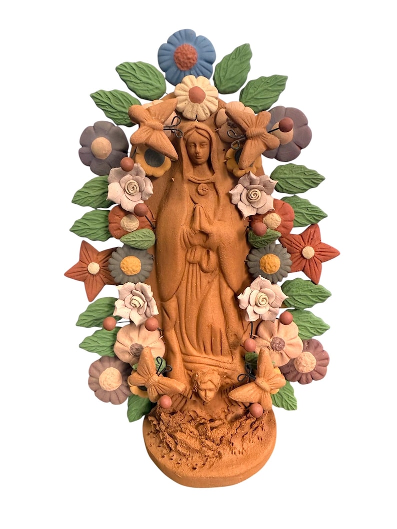 May include: A terracotta-colored religious statue of a woman, surrounded by colorful flowers, butterflies, and leaves. The statue has a detailed design and is set against a white background. The flowers are in shades of blue, pink, and orange.