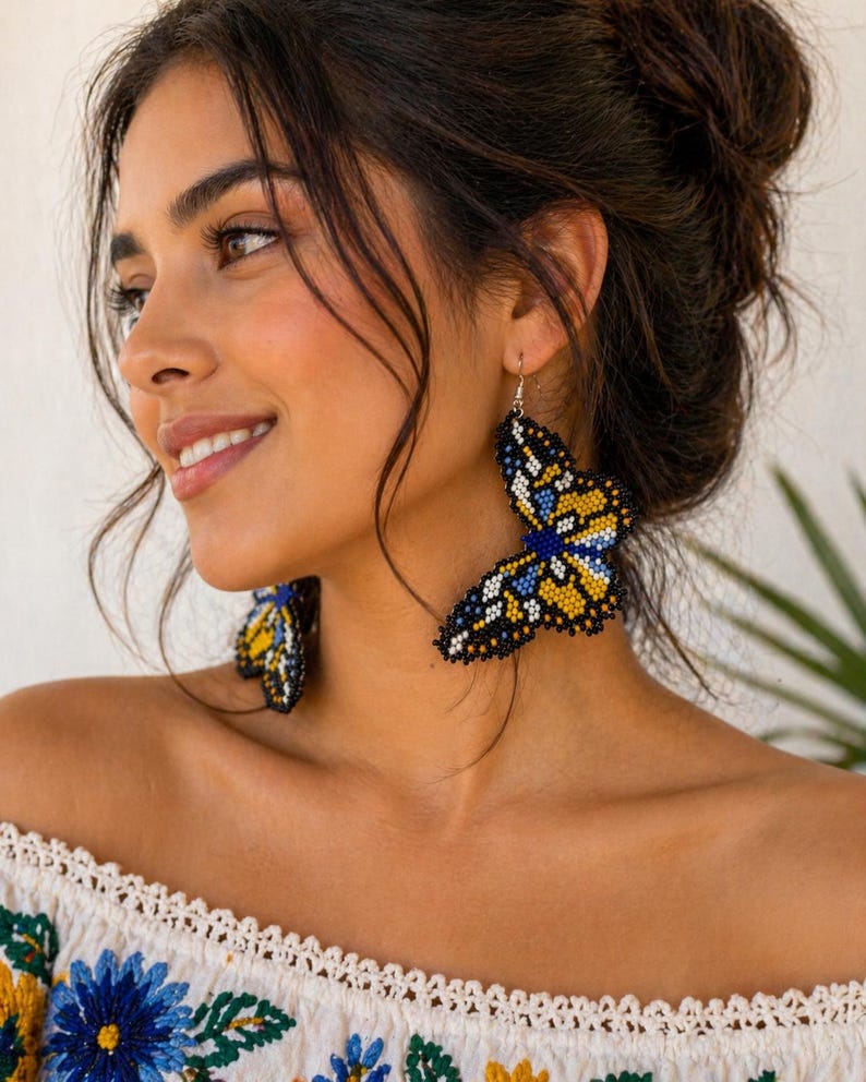 Op de afbeelding: Vlinder-vormige oorbellen van blauwe, gele en zwarte kralen. De oorbellen hangen aan zilveren haken. Een uniek accessoire, perfect om een vleugje fantasie aan elke outfit toe te voegen.