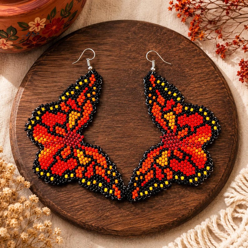 Op de afbeelding: Een paar handgemaakte vlinder oorbellen. De oorbellen hebben een levendig ontwerp met rode, oranje, gele en zwarte kralen. De vlindervleugels zijn gedetailleerd met een zwarte omtrek en zilveren haken.