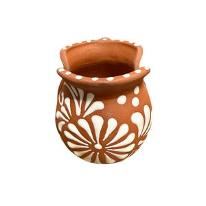 Op de afbeelding: Een kleine terracotta-kleurige keramische pot met een wit bloemmotief. De pot heeft een afgeronde body en een uitlopende rand met witte stippen. Het witte bloemmotief is symmetrisch en bedekt het grootste deel van het oppervlak van de pot.