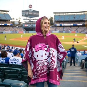 May include: A maroon hooded poncho featuring a Hello Kitty design wearing a Dodgers baseball cap and jersey. The poncho has a fringed hem and the words "Dodgers Los Angeles" are printed on the front. The background shows a baseball stadium.