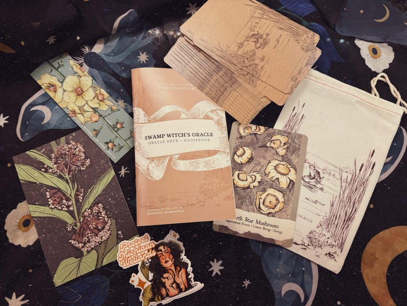 May include: An oracle deck and guidebook titled "Swamp Witch's Oracle" with accompanying cards, a drawstring bag, and stickers. The cards feature botanical illustrations and the guidebook is peach-colored. The items are arranged on a dark background with celestial patterns.