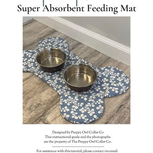 May include: A bone-shaped pet placemat featuring a blue fabric with a white leaf pattern. Two circular stainless steel bowls are placed on top of the mat. The text Pet Placemat Super Absorbent Feeding Mat is visible above the mat.